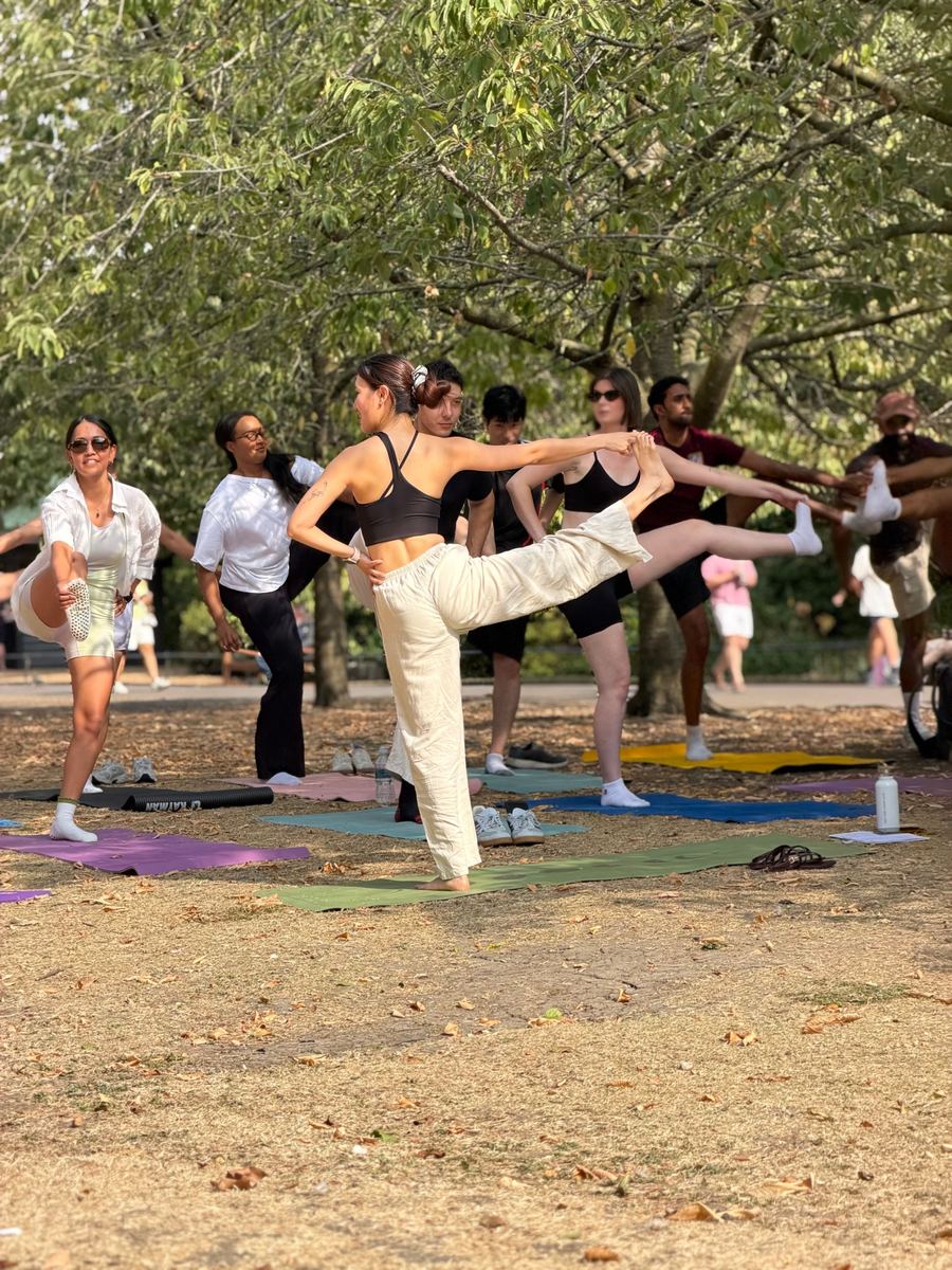 Zu leading the group in dancer pose under the trees